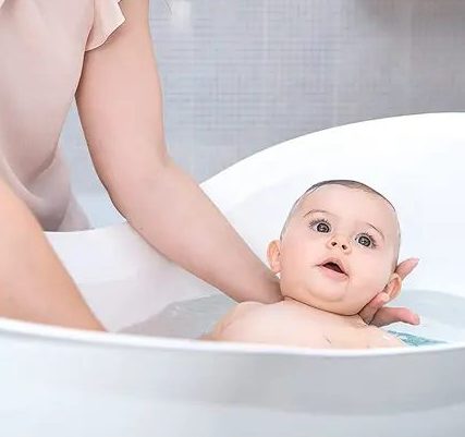 Bébé souriant dans son bain, tenu par sa maman