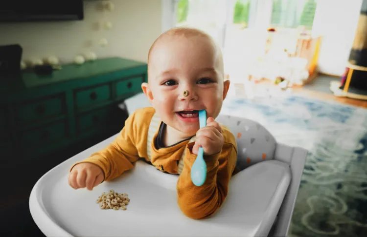 Bébé qui mange tout seul dans sa chaise haute