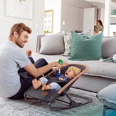 Papa qui joue avec son bébé installé dans un transat au salon