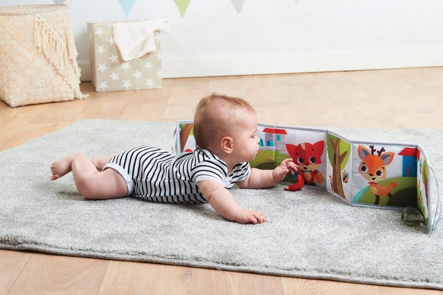 Bébé qui joue à plat ventre sur un tapis avec un livre d'éveil