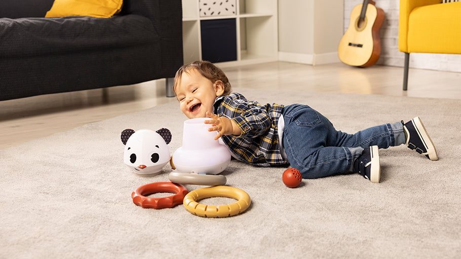 Petit garçon qui rit en jouant avec ses jouets d'éveil Tiny Love reçus en cadeau